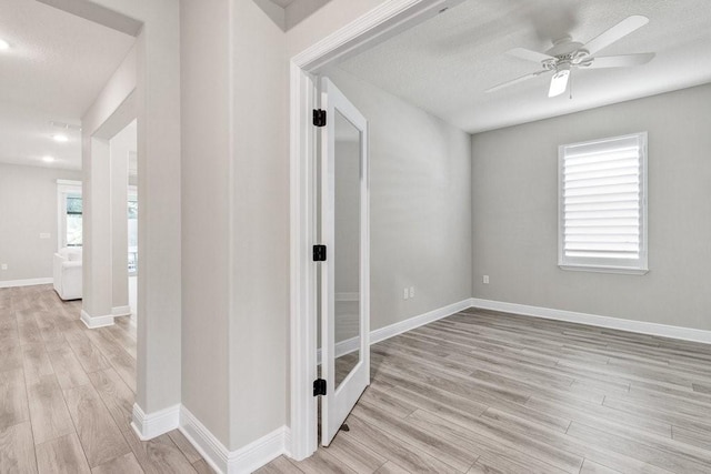 hallway with a healthy amount of sunlight, a textured ceiling, and light wood-type flooring