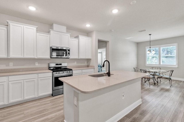 kitchen with white cabinets, sink, an island with sink, appliances with stainless steel finishes, and decorative light fixtures