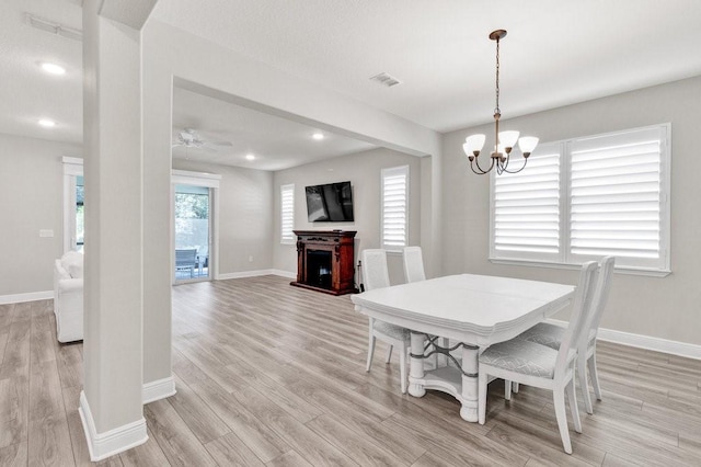 dining space with ceiling fan with notable chandelier and light hardwood / wood-style flooring