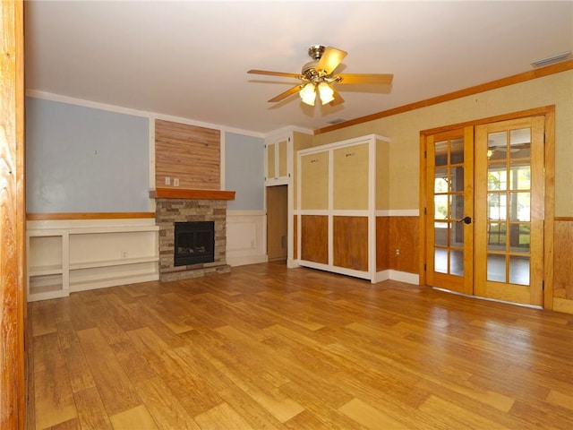 unfurnished living room with a fireplace, visible vents, light wood-style floors, french doors, and wainscoting