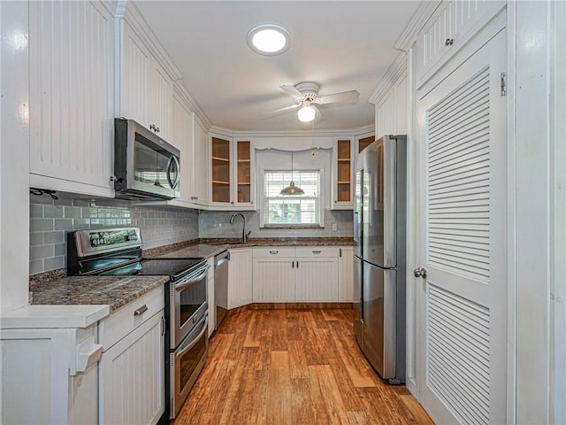 kitchen with white cabinetry, appliances with stainless steel finishes, decorative backsplash, light wood finished floors, and glass insert cabinets