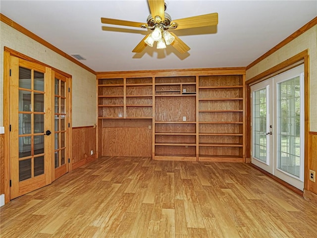 interior space featuring a wainscoted wall, visible vents, light wood-style floors, ornamental molding, and french doors