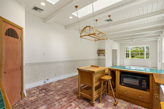 kitchen with hanging light fixtures, black microwave, beamed ceiling, a skylight, and ceiling fan