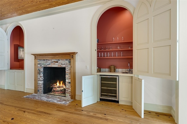 bar with a brick fireplace, light hardwood / wood-style floors, cream cabinets, beverage cooler, and sink