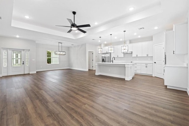 unfurnished living room with a tray ceiling, ceiling fan, and dark hardwood / wood-style flooring