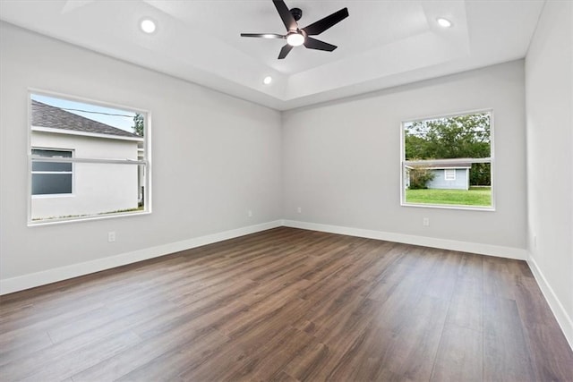 unfurnished room with a raised ceiling, ceiling fan, and dark wood-type flooring