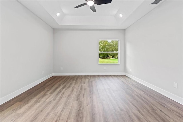 empty room featuring light wood-type flooring, a tray ceiling, and ceiling fan