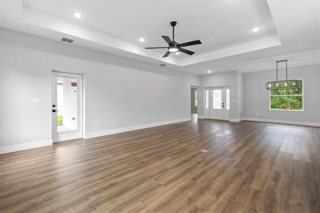 unfurnished living room featuring a raised ceiling, ceiling fan, and dark wood-type flooring