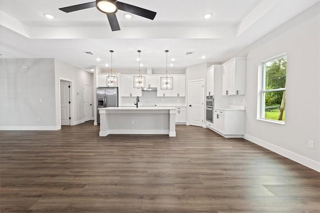 kitchen featuring appliances with stainless steel finishes, pendant lighting, dark hardwood / wood-style floors, white cabinetry, and an island with sink