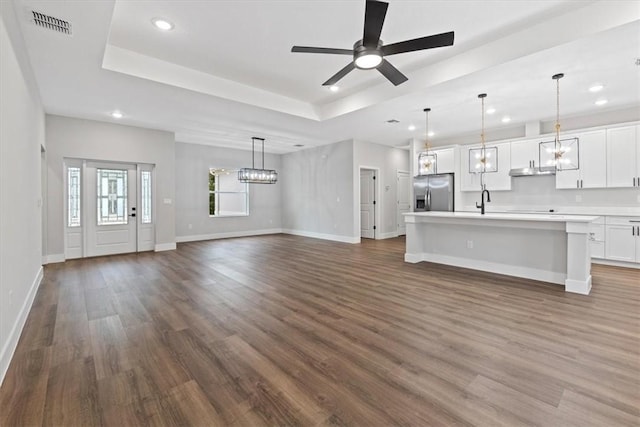 unfurnished living room featuring sink, ceiling fan, a raised ceiling, and dark wood-type flooring