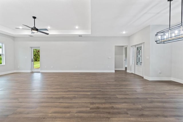 unfurnished living room featuring a tray ceiling, ceiling fan, and dark hardwood / wood-style floors