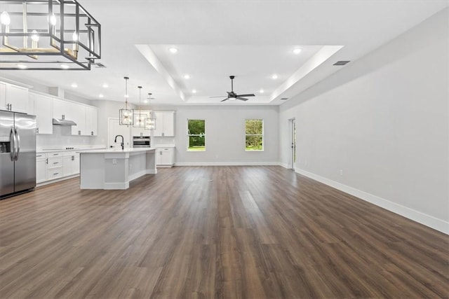 unfurnished living room with ceiling fan, sink, dark wood-type flooring, and a tray ceiling