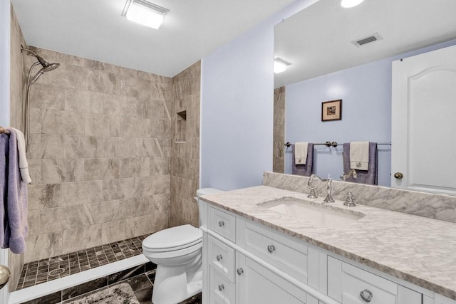 full bathroom featuring toilet, tiled shower, vanity, and visible vents