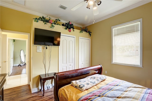 bedroom featuring multiple closets, crown molding, ceiling fan, and dark hardwood / wood-style floors