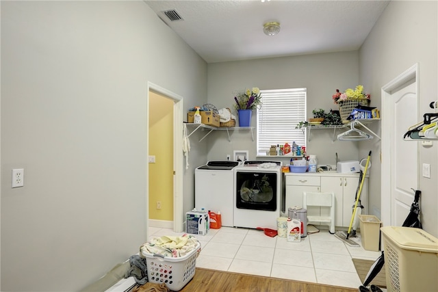 clothes washing area with washing machine and clothes dryer, cabinets, and light wood-type flooring