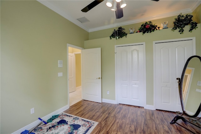 unfurnished bedroom with two closets, ceiling fan, dark hardwood / wood-style flooring, and ornamental molding