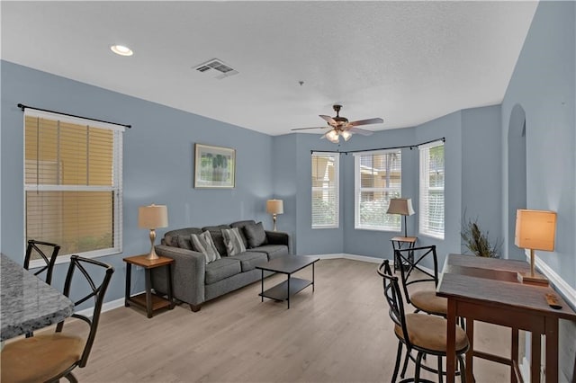 living room featuring ceiling fan, a textured ceiling, and light hardwood / wood-style floors