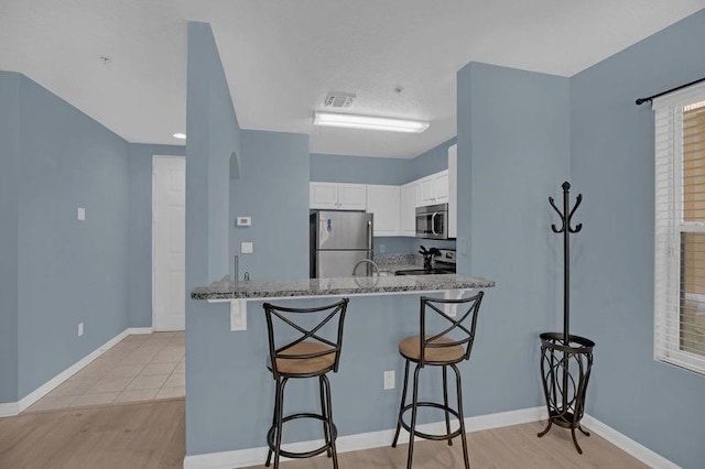 kitchen featuring appliances with stainless steel finishes, white cabinets, light stone countertops, a breakfast bar area, and light hardwood / wood-style flooring