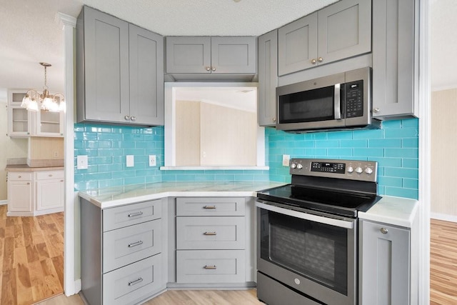 kitchen with light wood-type flooring, gray cabinetry, stainless steel appliances, and an inviting chandelier