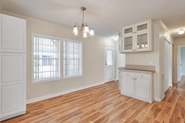 kitchen featuring pendant lighting, white cabinetry, ornamental molding, a notable chandelier, and light hardwood / wood-style flooring