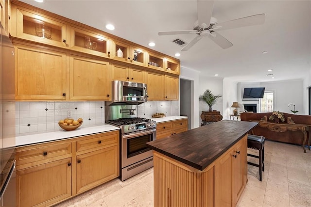 kitchen with appliances with stainless steel finishes, a breakfast bar, butcher block countertops, backsplash, and a center island