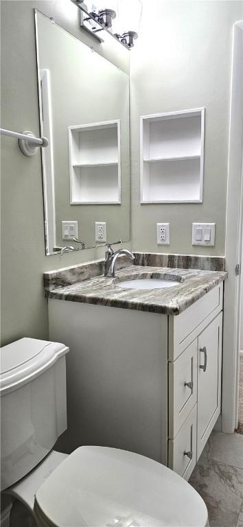 half bathroom with toilet, marble finish floor, and vanity