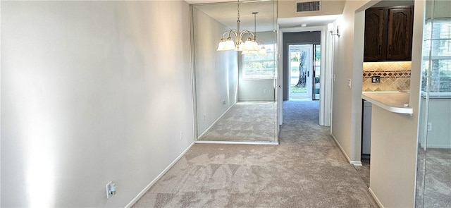 hallway featuring a chandelier, light colored carpet, plenty of natural light, and visible vents