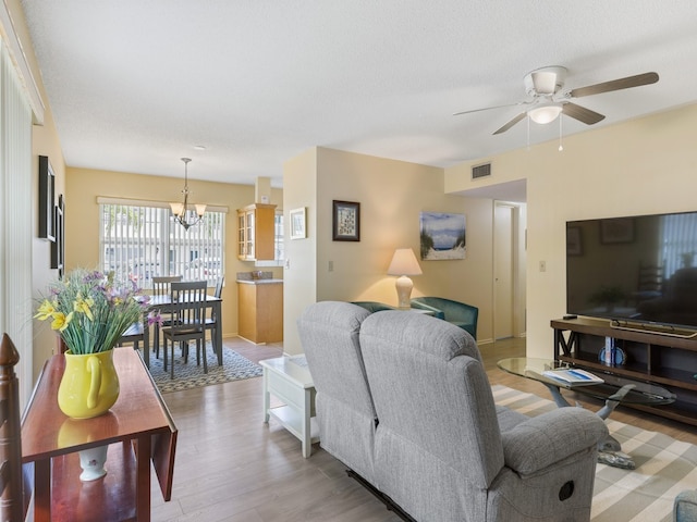 living room with light hardwood / wood-style floors and ceiling fan with notable chandelier