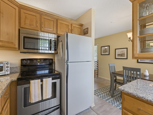 kitchen featuring light stone counters, a textured ceiling, light hardwood / wood-style flooring, white fridge, and black electric range oven