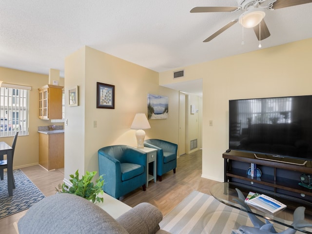 living room featuring ceiling fan, light hardwood / wood-style flooring, and a textured ceiling