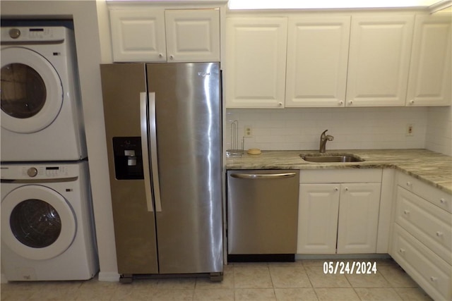 kitchen featuring stainless steel appliances, stacked washer and clothes dryer, white cabinets, and a sink