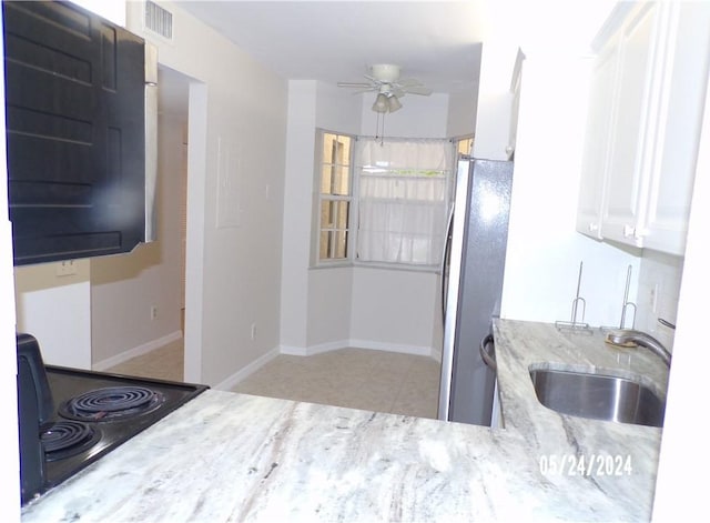 kitchen with a sink, freestanding refrigerator, light stone counters, ceiling fan, and range with electric cooktop