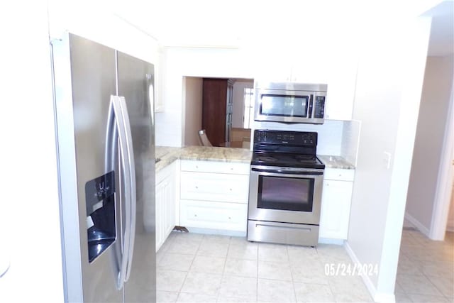 kitchen featuring appliances with stainless steel finishes, light tile patterned floors, white cabinets, and light stone countertops