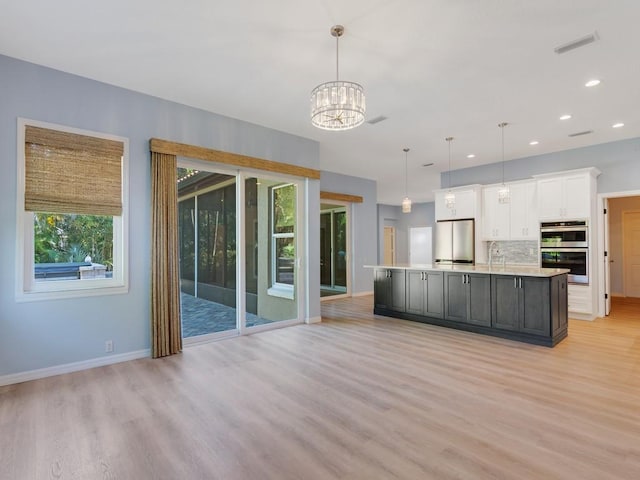 kitchen with white cabinetry, hanging light fixtures, stainless steel appliances, a center island with sink, and a chandelier