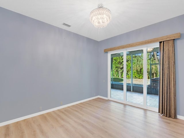 spare room featuring a notable chandelier and light hardwood / wood-style flooring