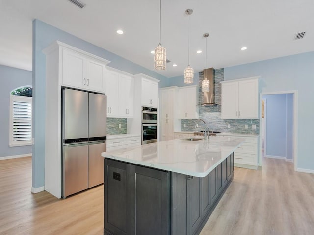 kitchen with wall chimney exhaust hood, white cabinetry, decorative light fixtures, appliances with stainless steel finishes, and a large island