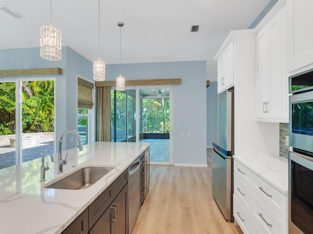 kitchen with white cabinetry, stainless steel appliances, decorative light fixtures, and sink