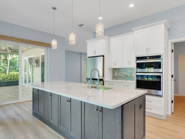 kitchen with stainless steel appliances, white cabinetry, light stone countertops, and a large island with sink