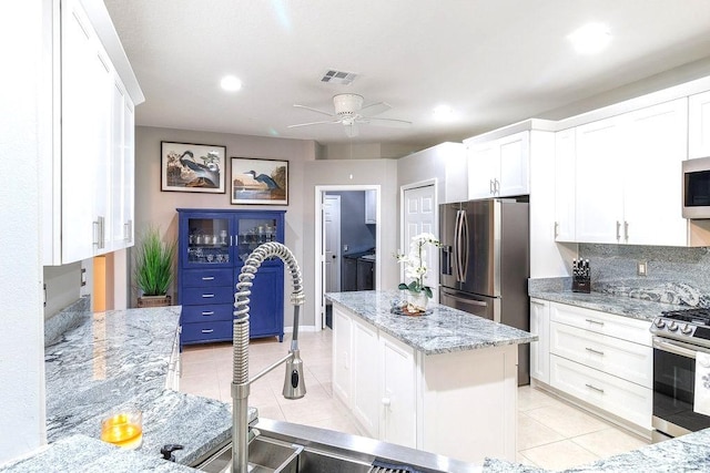 kitchen featuring light stone countertops, a center island, light tile patterned floors, white cabinets, and appliances with stainless steel finishes