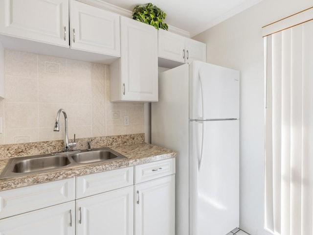 kitchen featuring sink, white refrigerator, ornamental molding, white cabinets, and decorative backsplash