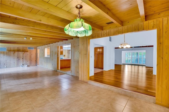 empty room with tile patterned flooring, wood walls, beam ceiling, and an inviting chandelier