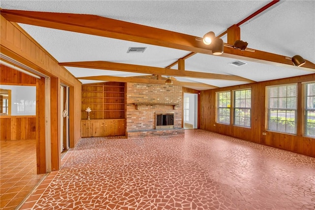 unfurnished living room with wooden walls, lofted ceiling with beams, a textured ceiling, and a brick fireplace