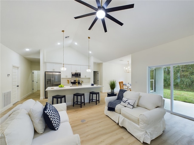 living room with ceiling fan with notable chandelier, light hardwood / wood-style floors, and high vaulted ceiling