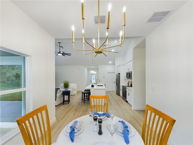 dining space with sink, ceiling fan with notable chandelier, and light wood-type flooring