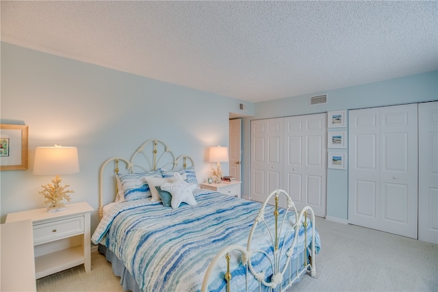 carpeted bedroom featuring a textured ceiling and two closets