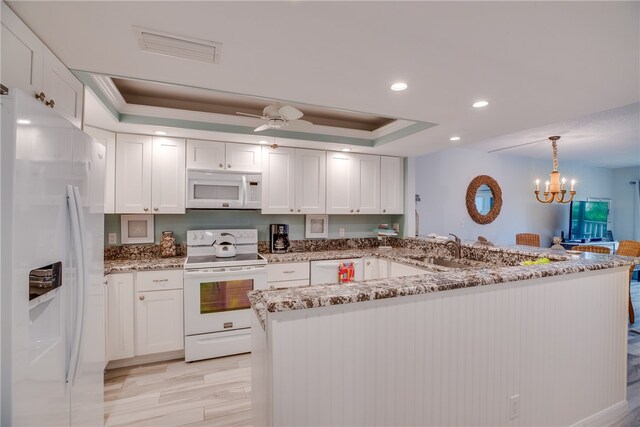 kitchen featuring white cabinetry, decorative light fixtures, a tray ceiling, white appliances, and light wood-type flooring