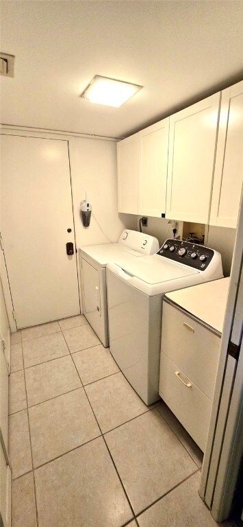 washroom featuring washing machine and dryer, light tile patterned floors, and cabinets