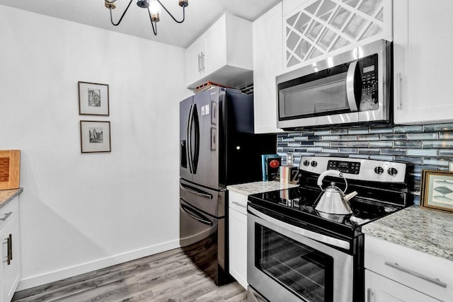 kitchen featuring tasteful backsplash, white cabinetry, stainless steel appliances, light stone countertops, and light hardwood / wood-style flooring