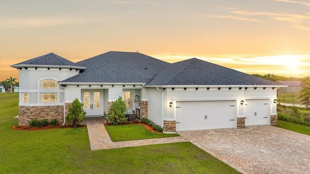 view of front facade with stucco siding, a lawn, driveway, french doors, and a garage