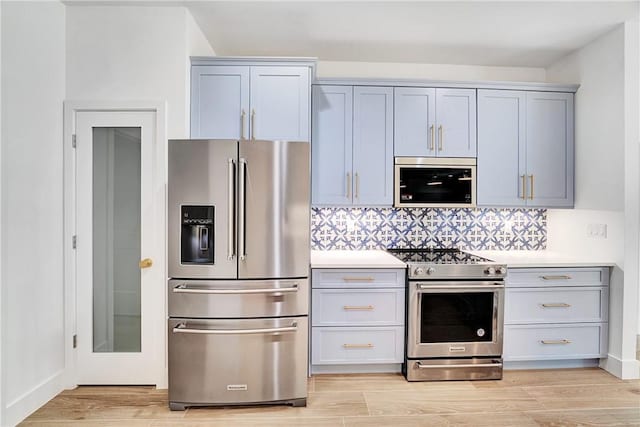 kitchen featuring light countertops, decorative backsplash, gray cabinets, light wood-style floors, and stainless steel appliances